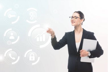 gülümseyen iş kadını dizüstü bilgisayar tutarak ve gri arka plan üzerinde güvenlik simgeleri ve multimedya pictogramlar parmak ile işaret