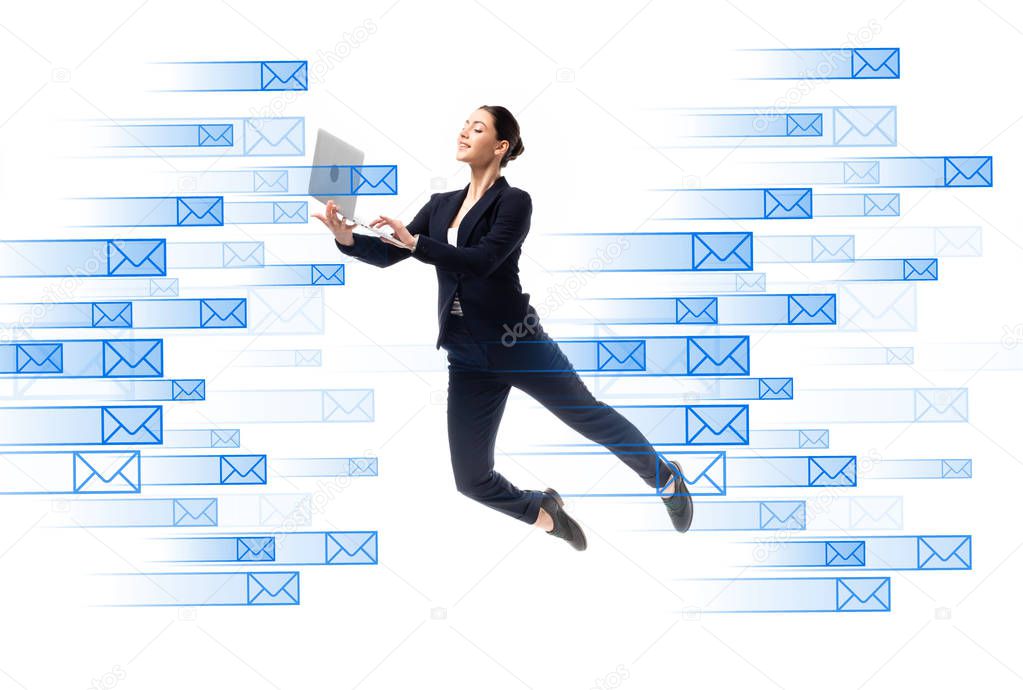 young businesswoman using laptop while levitating near e-mail icons isolated on white