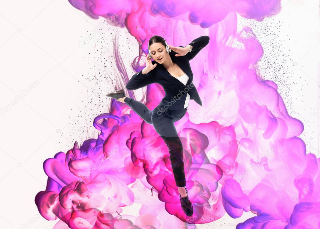 young businesswoman dancing in headphones on background with pink and purple smoke splashes isolated on white