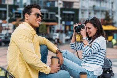 Kadın oturma ve güneş gözlüğü ve kahve fincanı içinde çok ırklı adam fotoğraf çekmek