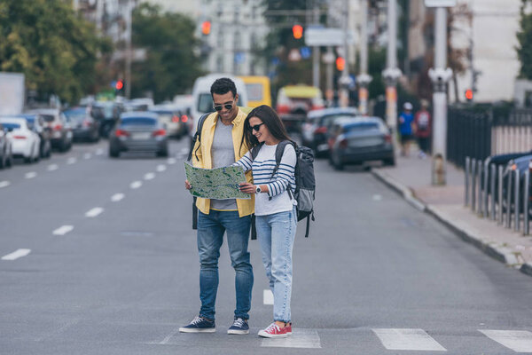 Женщина и многорасовый друг с рюкзаками держат карту города на пешеходном переходе
