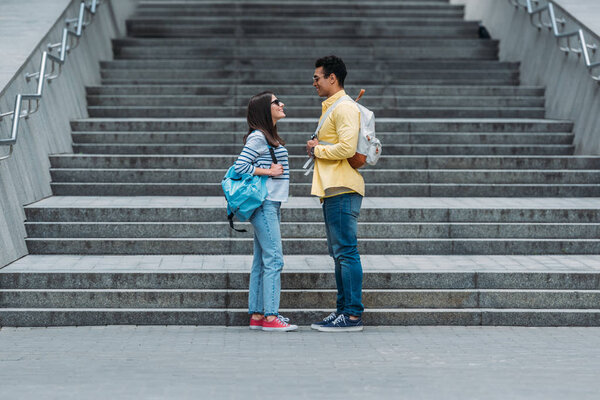 Woman standing in front of stairs and looking at bi-racial friend with backpack