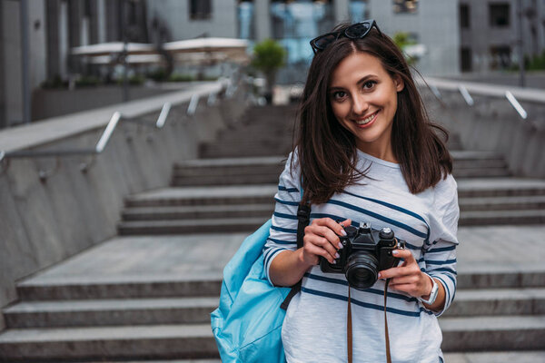 Woman in casual with backpack holding digital camera and smiling