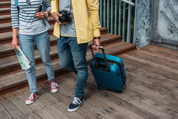 cropped view of multicultural woman and man walking with blue luggage 
