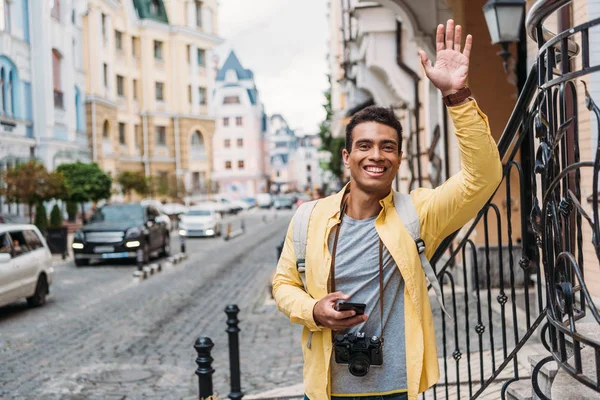 Happy Mixed Race Man Holding Smartphone While Waving Hand — Stock Photo, Image