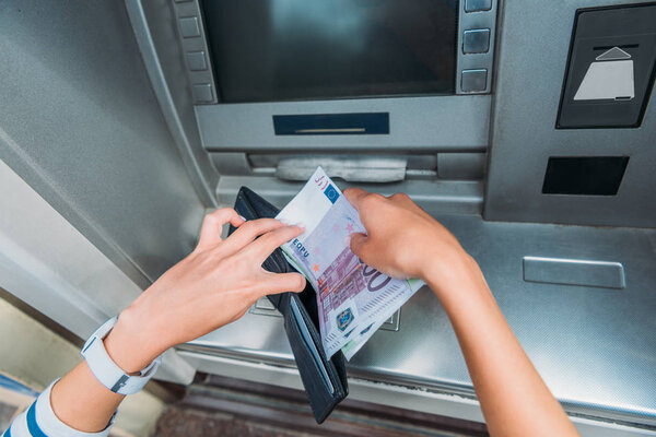 top view of woman putting money in wallet near atm machine 