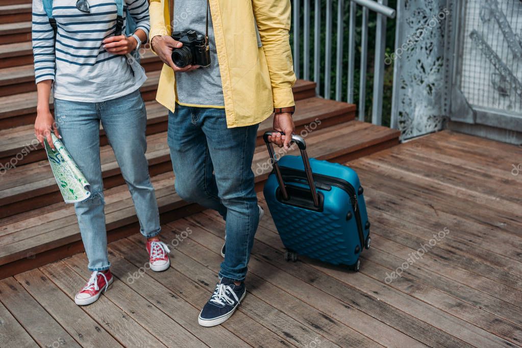 cropped view of multicultural woman and man walking with blue luggage 