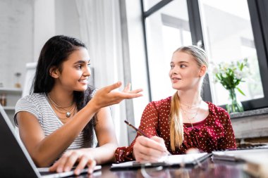 selective focus of multicultural friends smiling and talking in apartment 