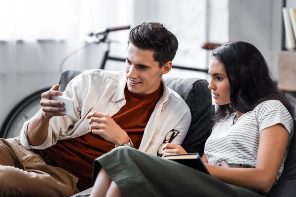 Estudiantes Multiculturales Sosteniendo Libro Usando Smartphone Apartamento — Foto de Stock