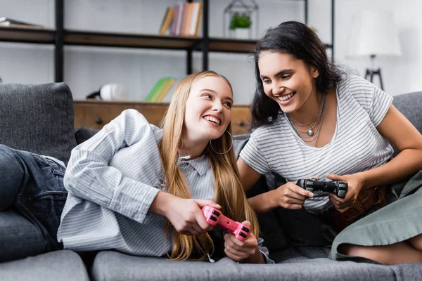 Kiev, Ukrayna - 10 Temmuz 2019: Kanepede oturan ve dairede video oyunu oynayan çok kültürlü arkadaşlar 