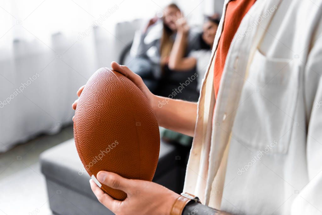 Selective focus of man holding Rugby Ball in apartment