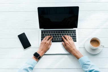 akıllı telefon ve kahve fincan ı yakınında dizüstü bilgisayarda yazarak kadın üst görünümü 