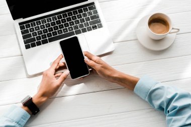 dizüstü bilgisayar ve kahve fincan yakınında boş ekran ile akıllı telefon tutan kadın üst görünümü 