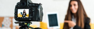 panoramic shot of digital camera with happy video blogger pointing with finger at digital tablet with blank screen  clipart