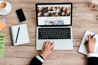 KYIV, UKRAINE - JULY 23, 2019: top view of woman using laptop with depositphotos website near smartphone with blank screen clipart