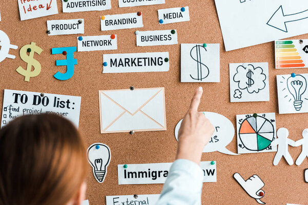 cropped view of businesswoman pointing with finger at sticky notes on notice board