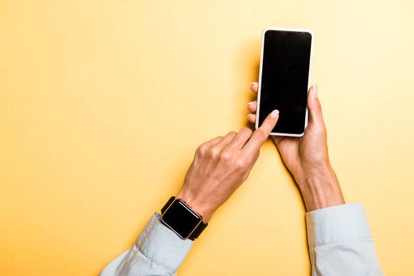 cropped view of woman pointing with finger at smartphone with blank screen on orange