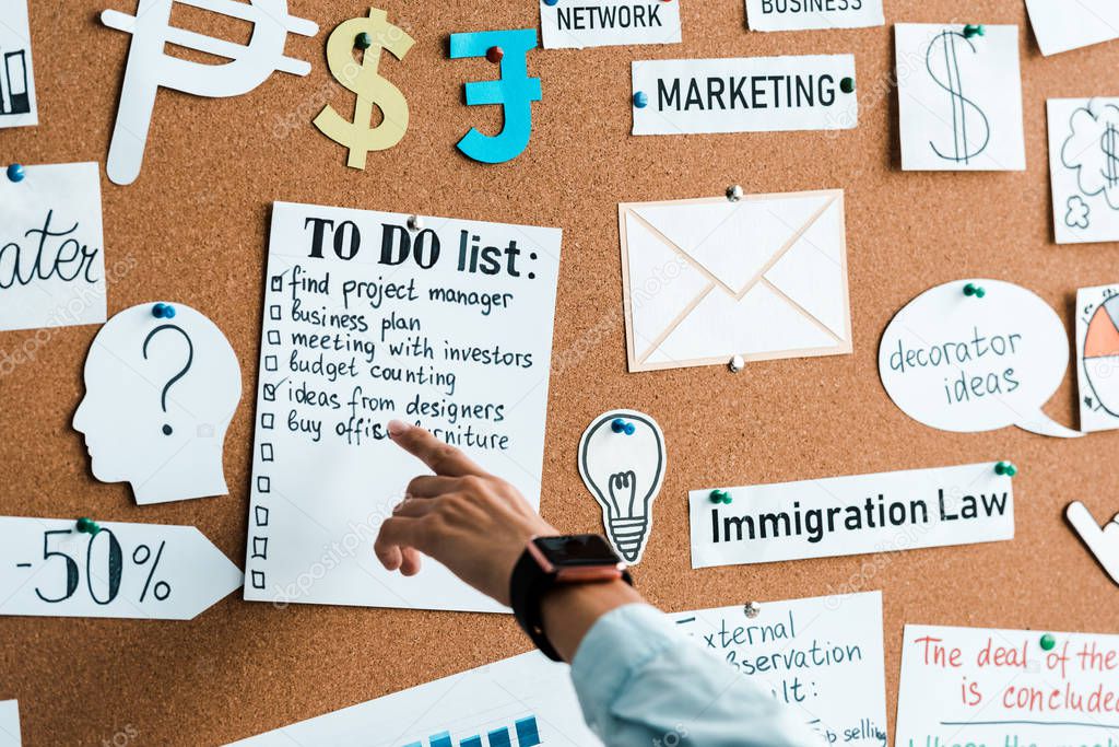 cropped view of businesswoman pointing with finger at to do list near lettering on notice board