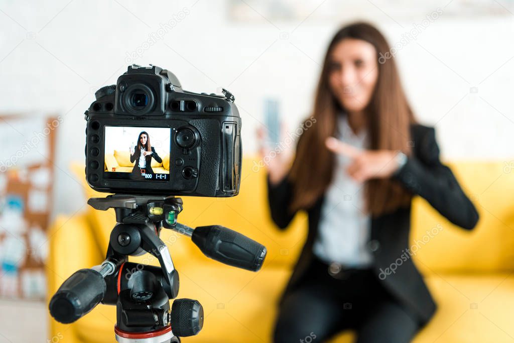 selective focus of digital camera with happy video blogger pointing with finger at smartphone 