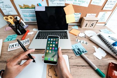 Kiev, Ukrayna - 23 Temmuz 2019: boş ekranlı dizüstü bilgisayarın, yapışkan notların ve dizüstü bilgisayarın yanında iphone tutan iş kadınının kırpılmış görünümü 