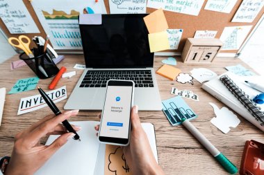 Kiev, Ukrayna - 23 Temmuz 2019: boş ekranlı yazı ve dizüstü bilgisayar ile yapışkan notlar yakınında messenger uygulaması ile akıllı telefon tutan kadının kırpılmış görünümü 
