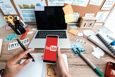 Kiev, Ukrayna - 23 Temmuz 2019: boş ekranlı yazı ve dizüstü bilgisayar ile yapışkan notlar yakınında youtube uygulaması ile akıllı telefon tutan kadın kırpılmış görünümü 