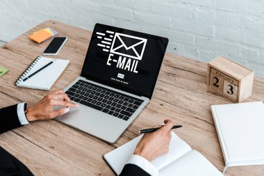 boş ekranlı akıllı telefonun yakınında e-posta yazısı ile dizüstü bilgisayar kullanırken kalem tutan kadının kırpılmış görünümü 