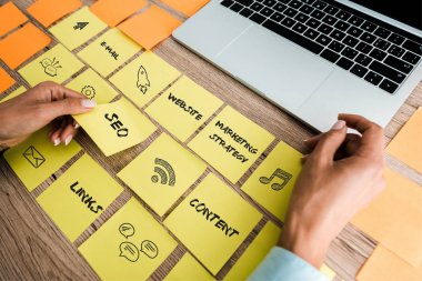 cropped view of woman touching sticky note with seo lettering near laptop on desk  clipart