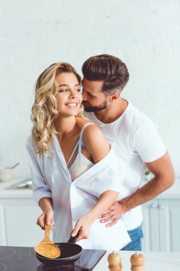 yakışıklı genç adam sarılma mutlu kız arkadaşı kızartma tavası üzerinde pancake pişirme 