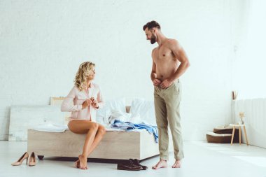 yatak odasında giyinirken birbirlerine bakan gülümseyen genç çift