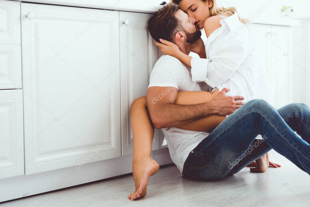 young couple hugging and kissing while sitting on floor in kitchen
