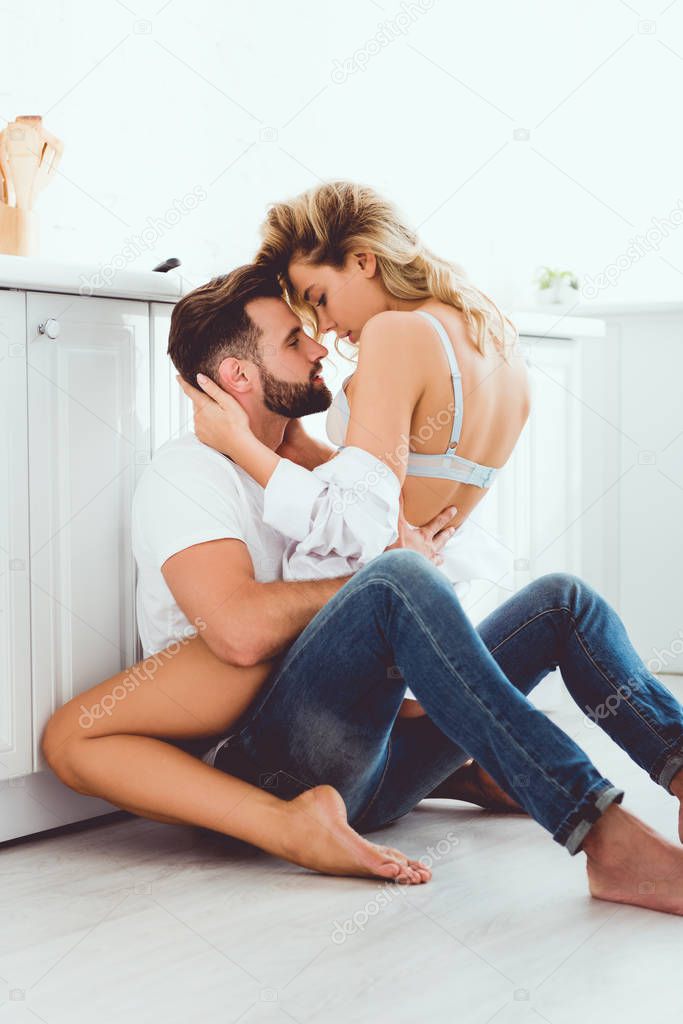 young couple embracing while sitting on floor in kitchen