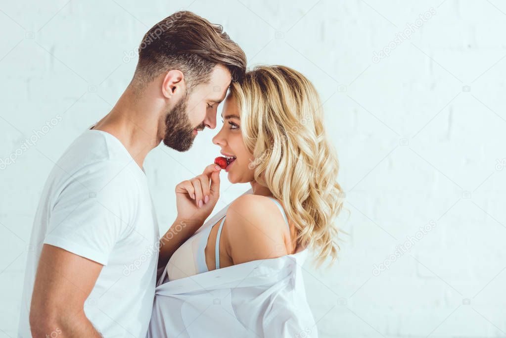 handsome young man hugging beautiful girlfriend tasting strawberry