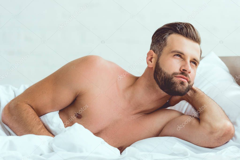 handsome, shirtless sexy man lying in bed and looking away