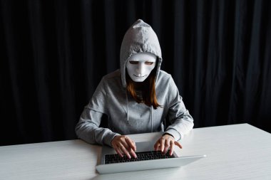 anonymous internet troll in mask typing on laptop keyboard on black clipart