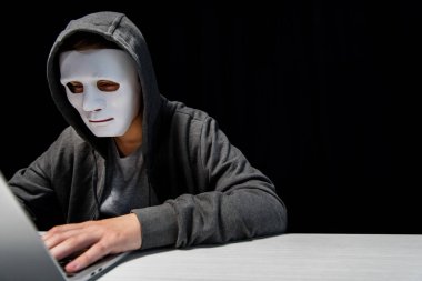 anonymous internet troll in mask typing on laptop keyboard isolated on black clipart
