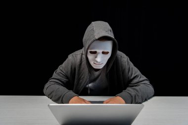 anonymous internet troll in mask typing on laptop keyboard isolated on black clipart