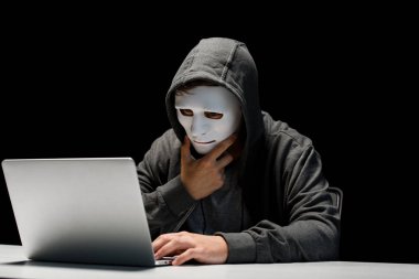 anonymous internet troll in mask typing on laptop keyboard isolated on black clipart