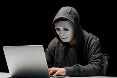 anonymous internet troll in mask typing on laptop keyboard isolated on black clipart
