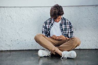 çapraz bacaklar ile oturan ve akıllı telefon kullanarak genç ön görünümü