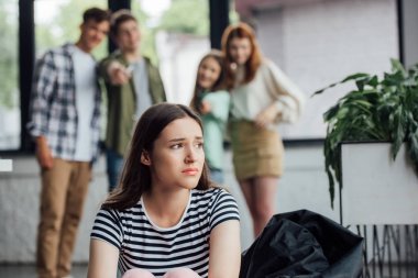 selective focus of group of teenagers bullying sad girl in school clipart