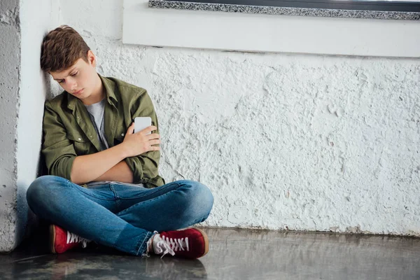 Λυπημένος Έφηβος Κάθεται Σταυρωτά Πόδια Και Κρατώντας Smartphone — Φωτογραφία Αρχείου