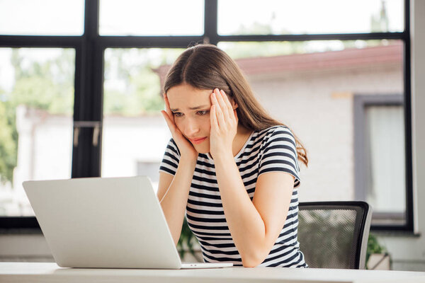 sad girl in striped t-shirt using laptop at home