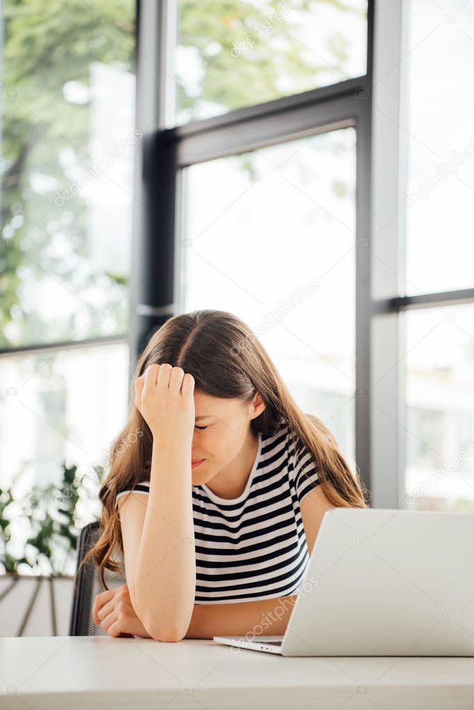 sad girl in striped t-shirt using laptop at home