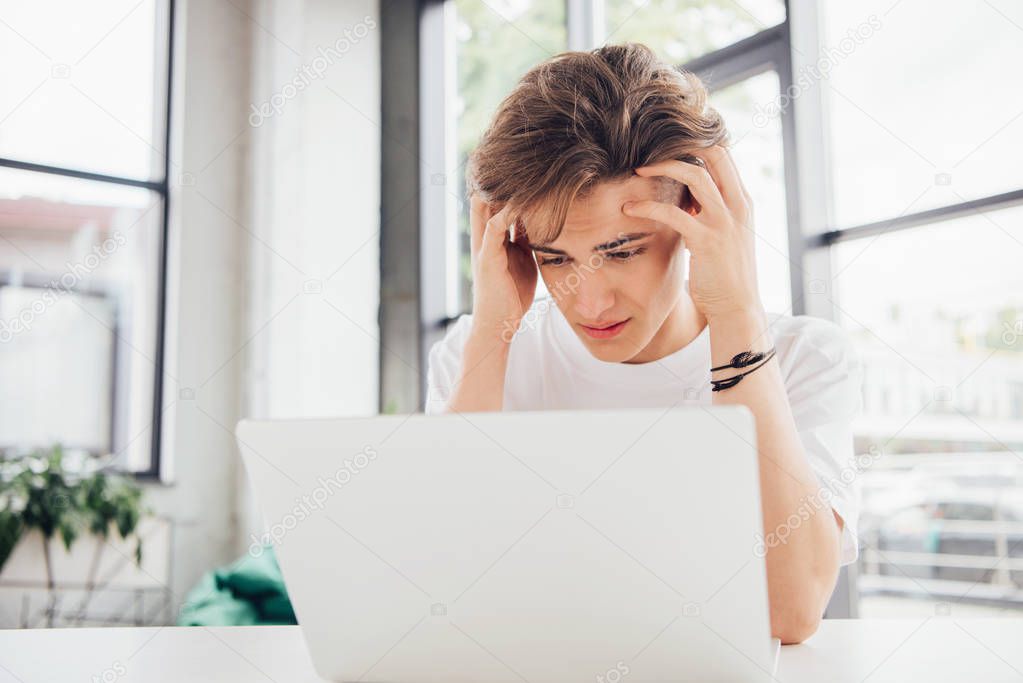 sad teen boy in white t-shirt using laptop at home