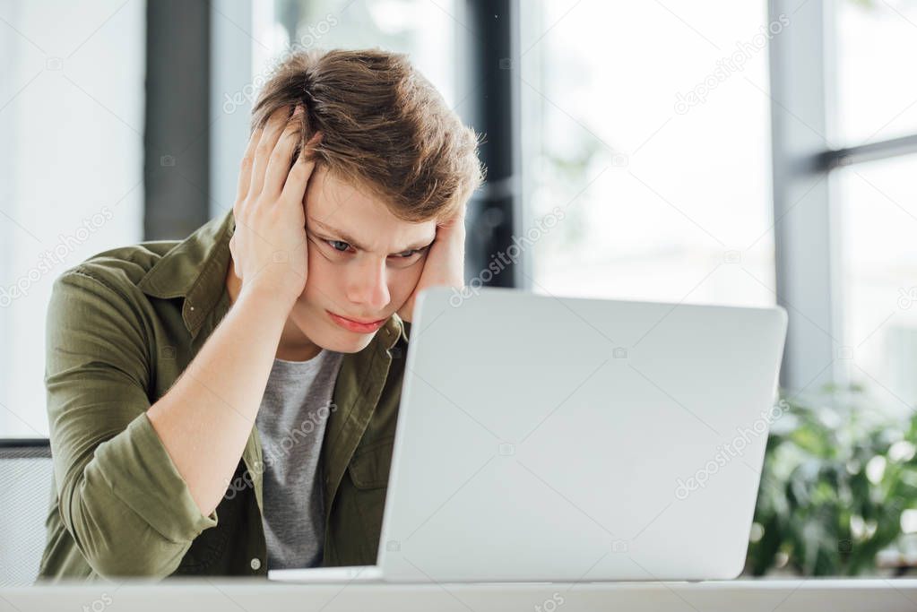 focused teen boy sitting at table and using laptop at home