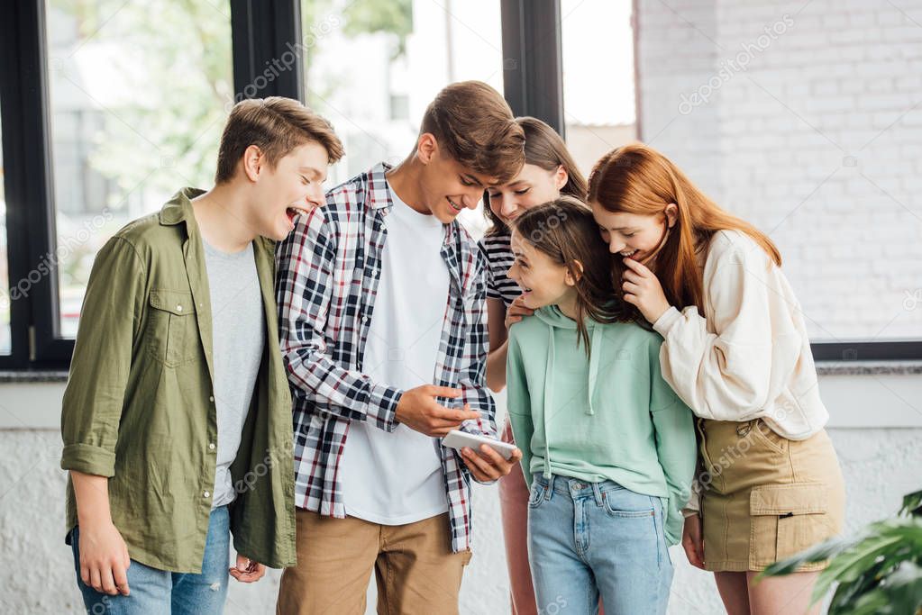 group of happy friends laughing while using smartphone