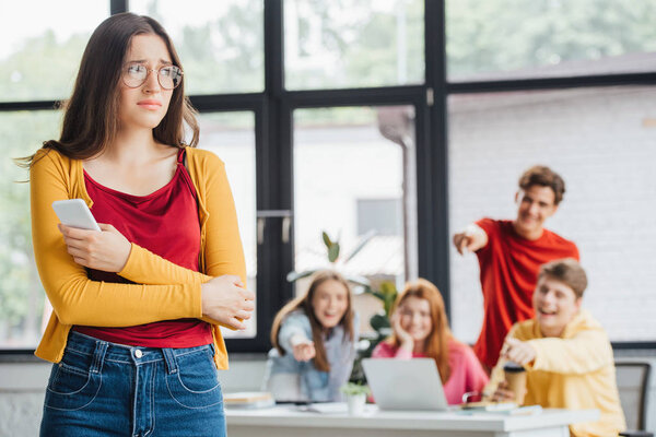 group of schoolchildren bullying sad girl with smartphone