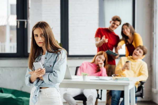 group of schoolchildren laughing at sad girl with smartphone