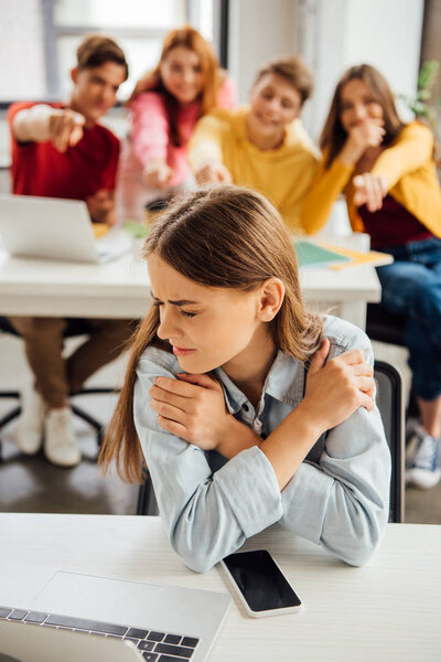 schoolchildren laughing while bullying sad girl on foreground